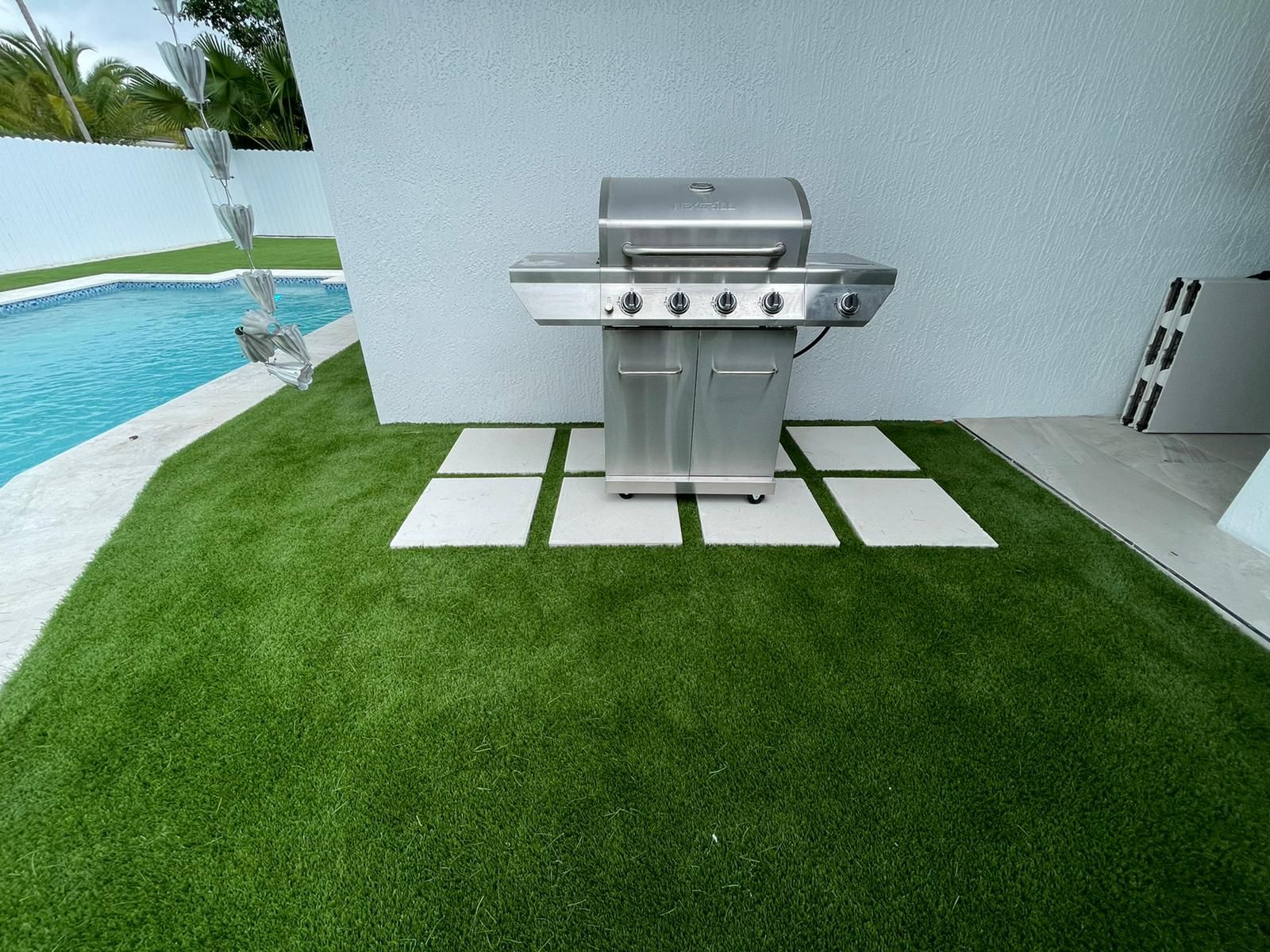 A stainless steel grill is sitting on top of a lush green lawn next to a pool.