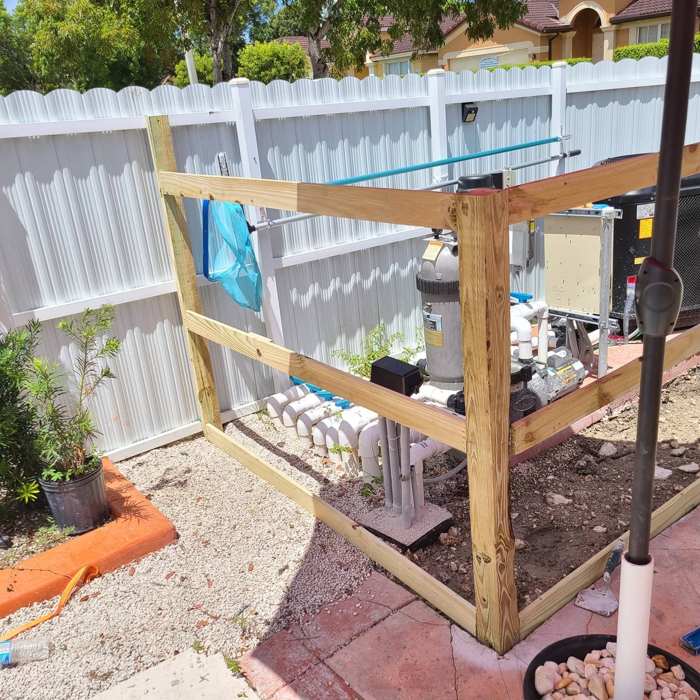 A wooden fence is surrounding a pool pump in a backyard.
