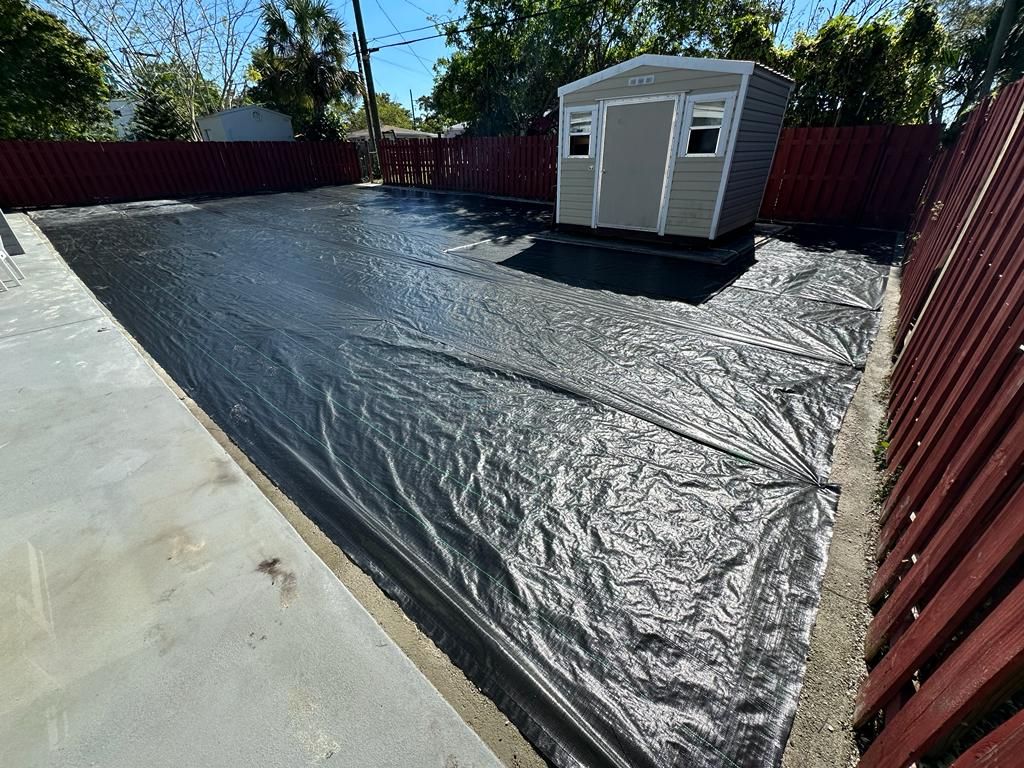 A shed is sitting on top of a black tarp in a backyard.