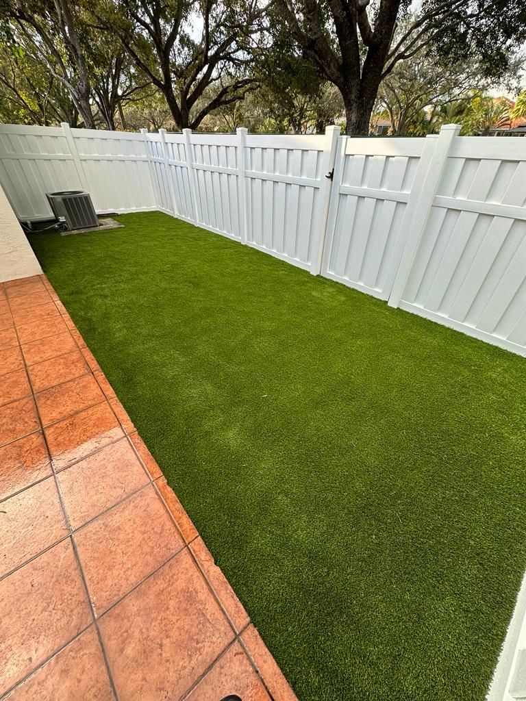 A backyard with a white fence and artificial grass.