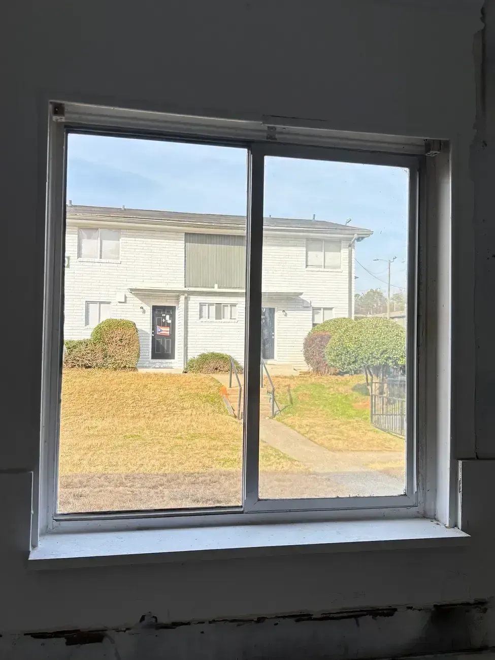 View through a window to a white house and front yard on a sunny day