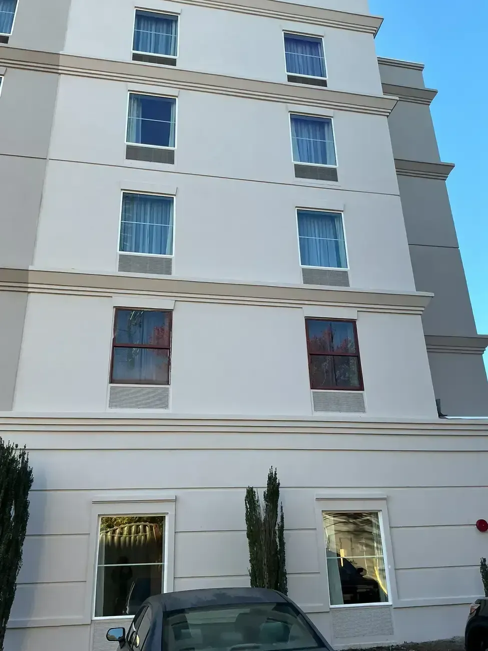 White multi-story apartment building with blue-trimmed windows and parked car in front