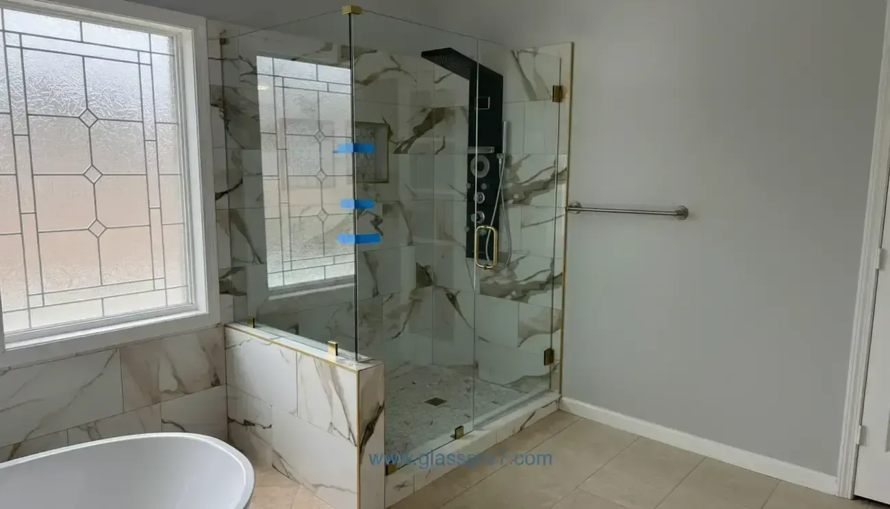 Modern bathroom with glass shower, marble tile, window, and bathtub edge.