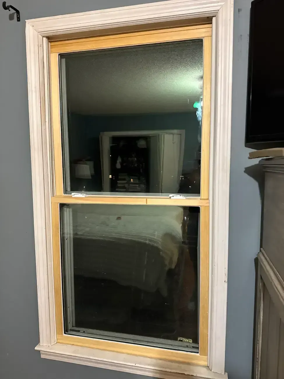 Wooden-framed window in a gray wall, reflecting a bedroom interior at night.