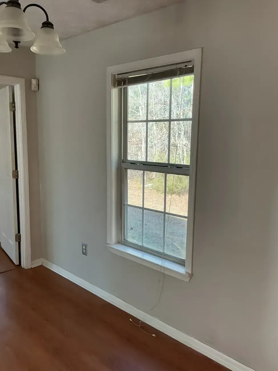 Empty room with hardwood floor, white walls, and a sunlit window with blinds