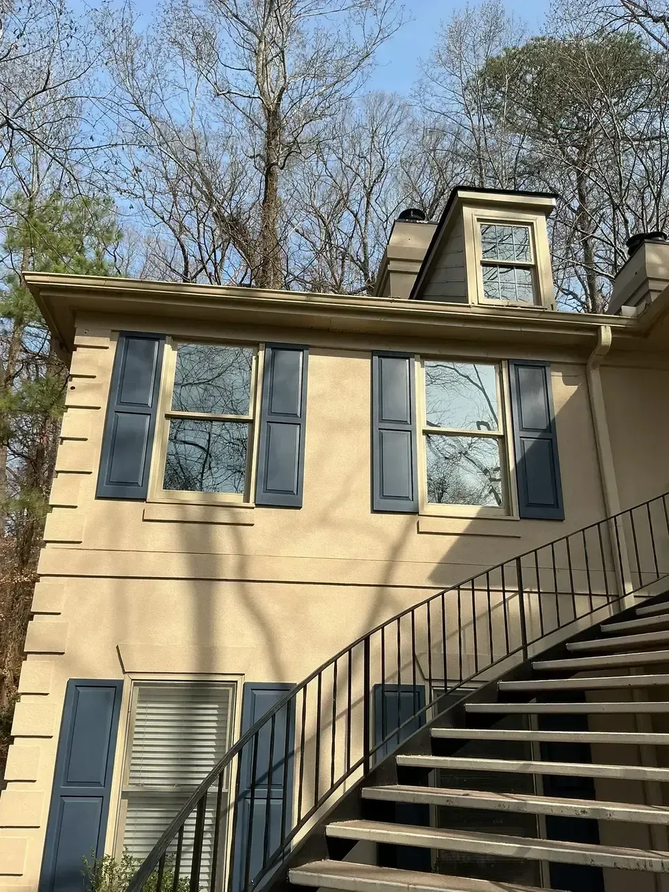 Beige house with blue shutters beside outdoor stairs under leafless trees