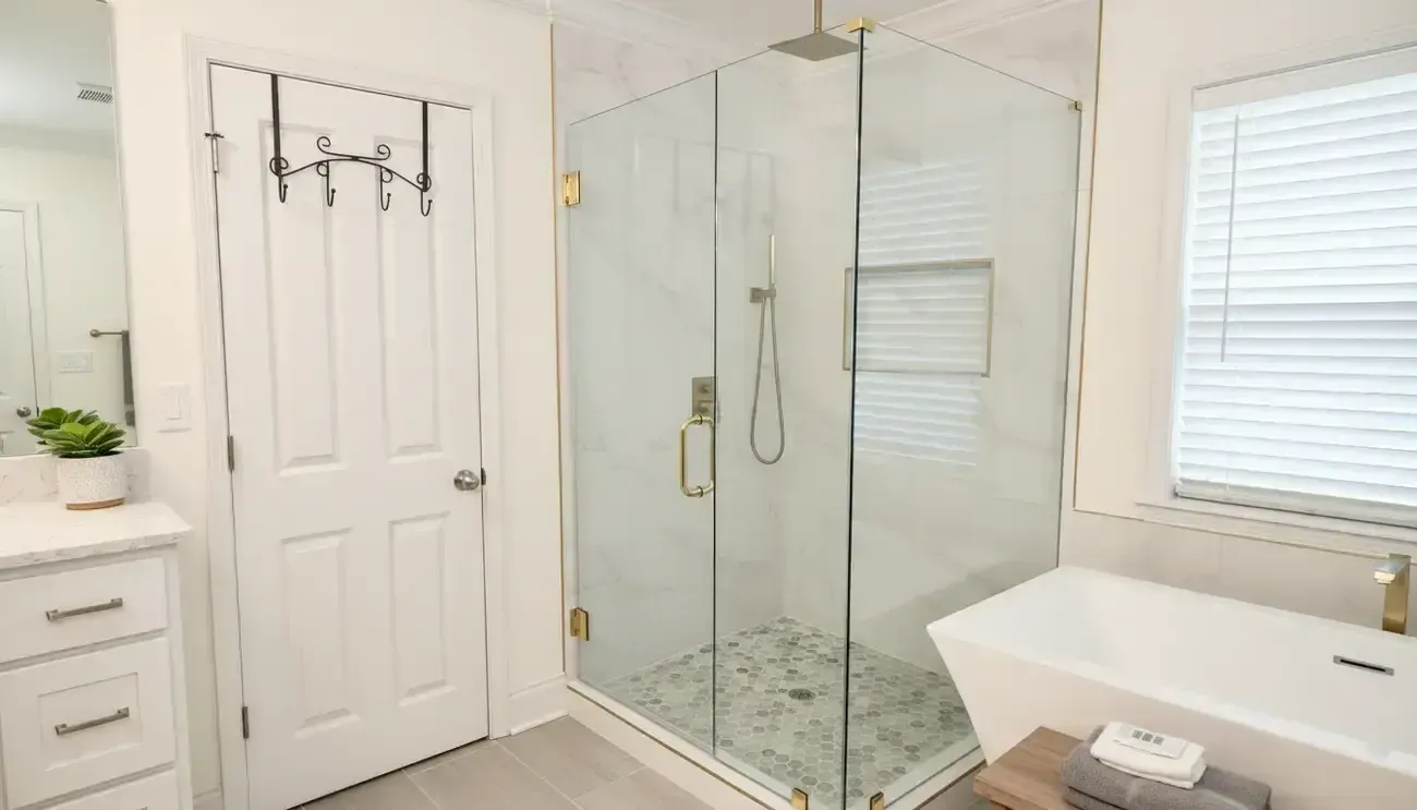 Bright white bathroom with glass shower, vanity, toilet, and window blinds