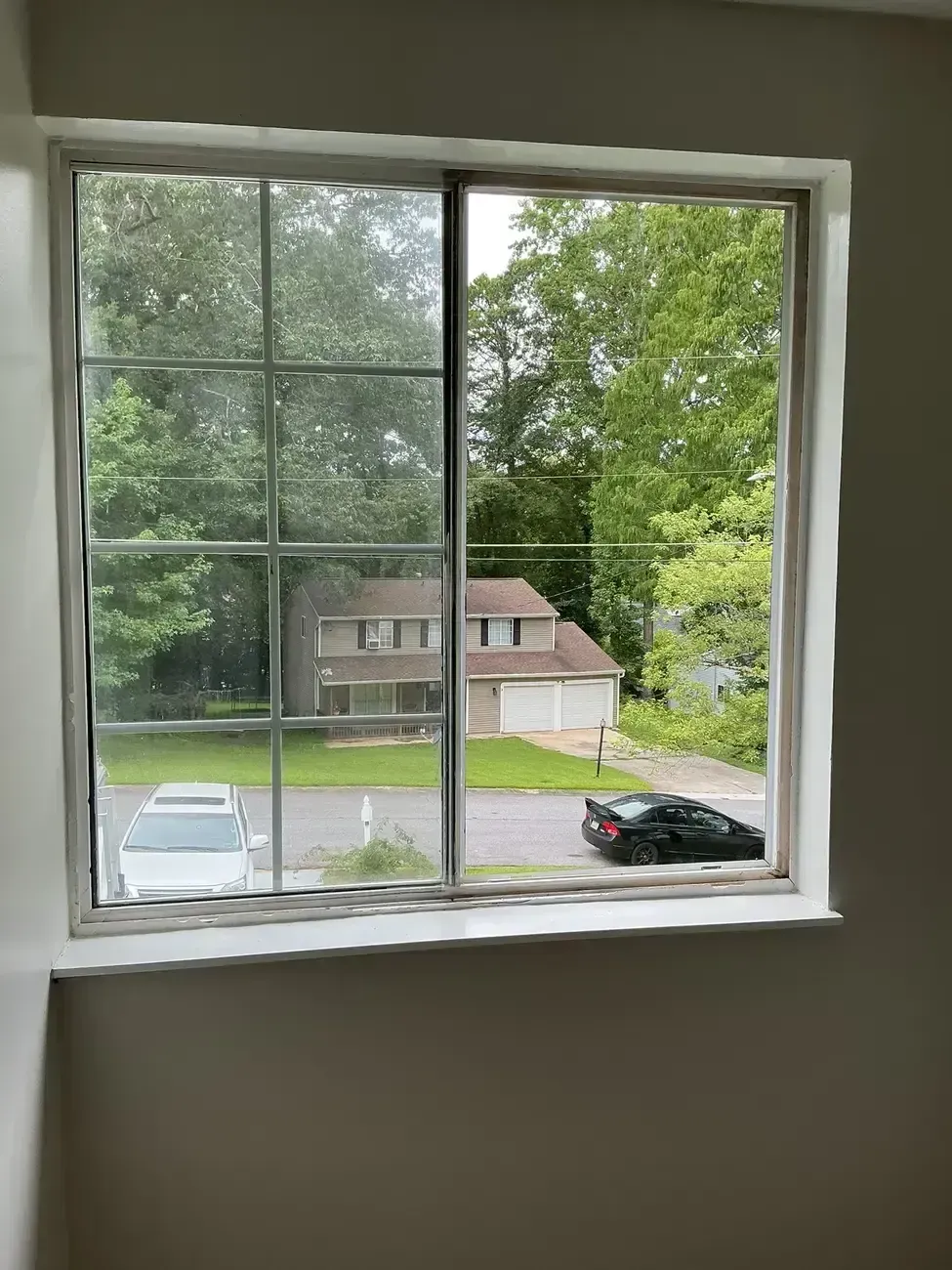 View through a white-paned window of a suburban street, house, trees, and parked cars