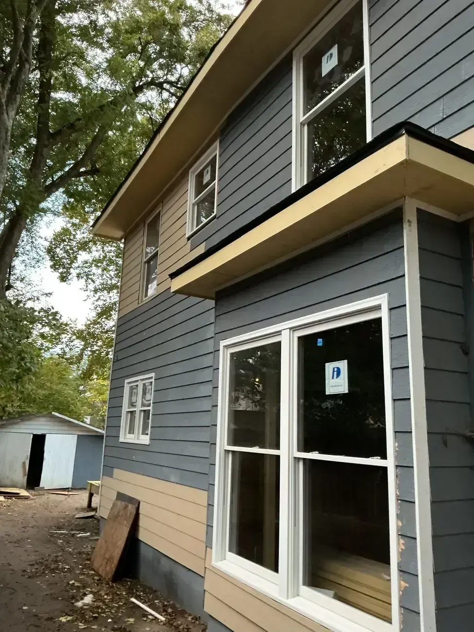 Gray two-story house exterior with white-framed windows and a small outbuilding nearby.