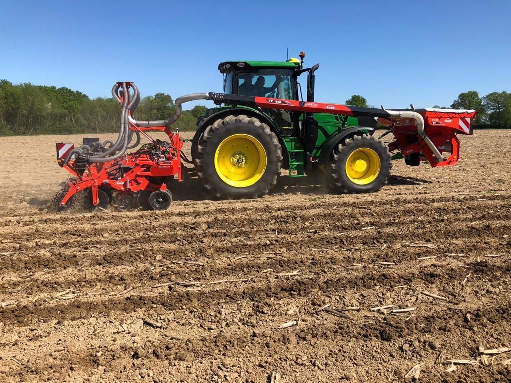 Ein grüner und gelber Traktor mit roten Anbaugeräten pflügt an einem sonnigen Tag ein Feld.