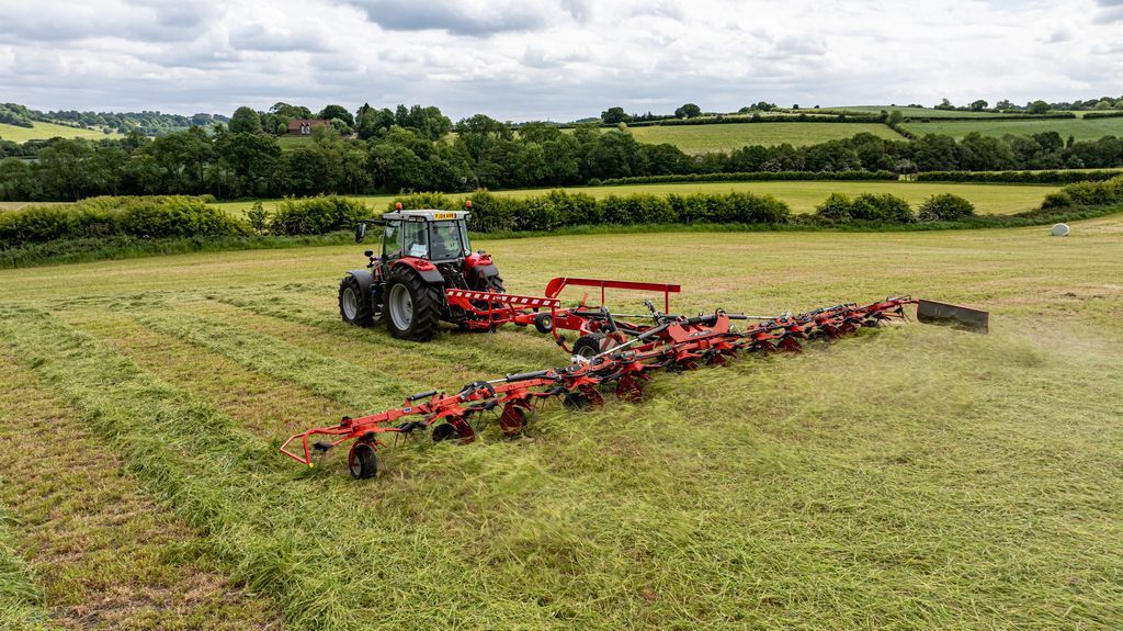 Ein roter Traktor zieht eine breite Sämaschine über ein Feld, der Himmel ist bedeckt.