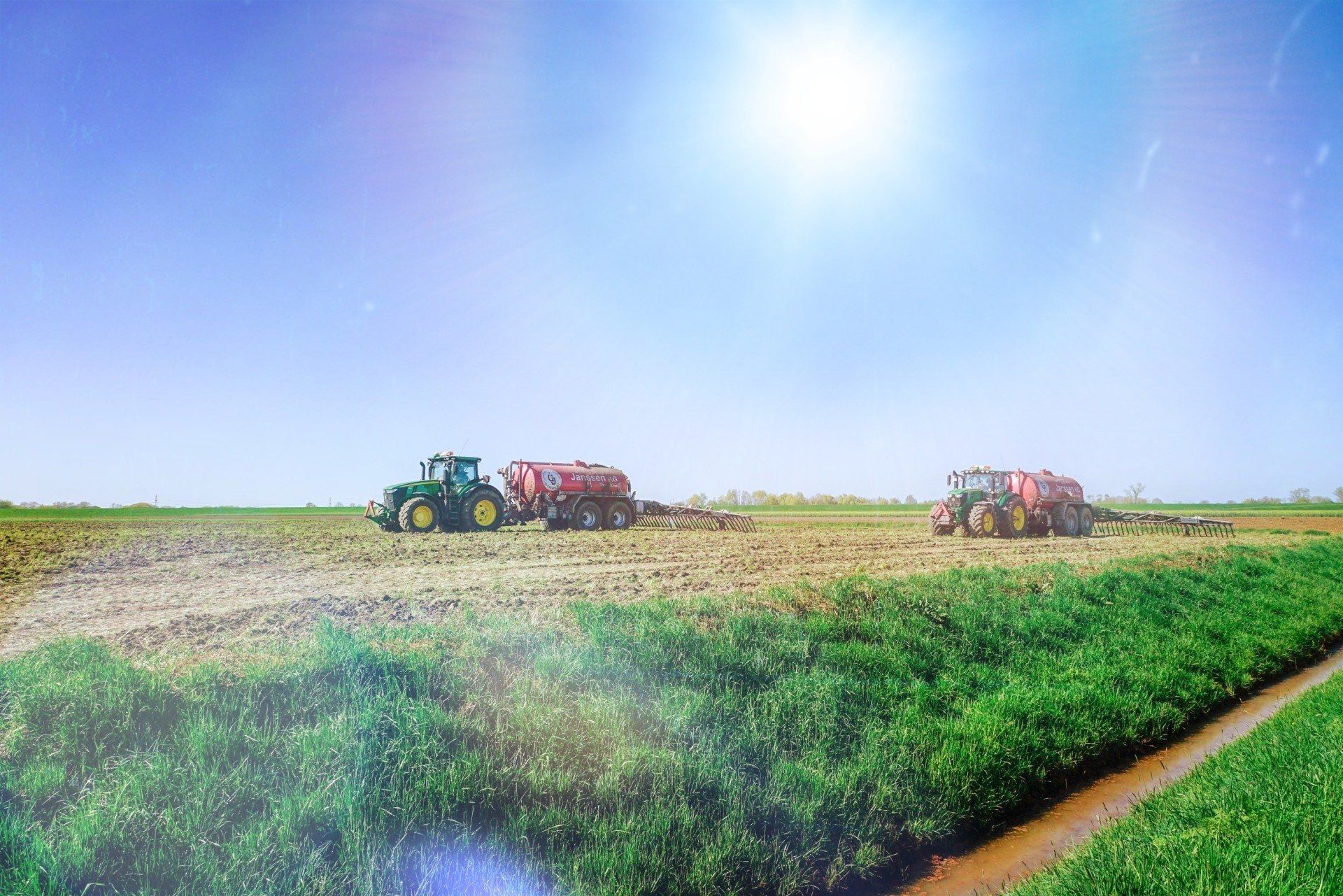 An einem sonnigen Tag arbeiten zwei Traktoren auf einem Feld.