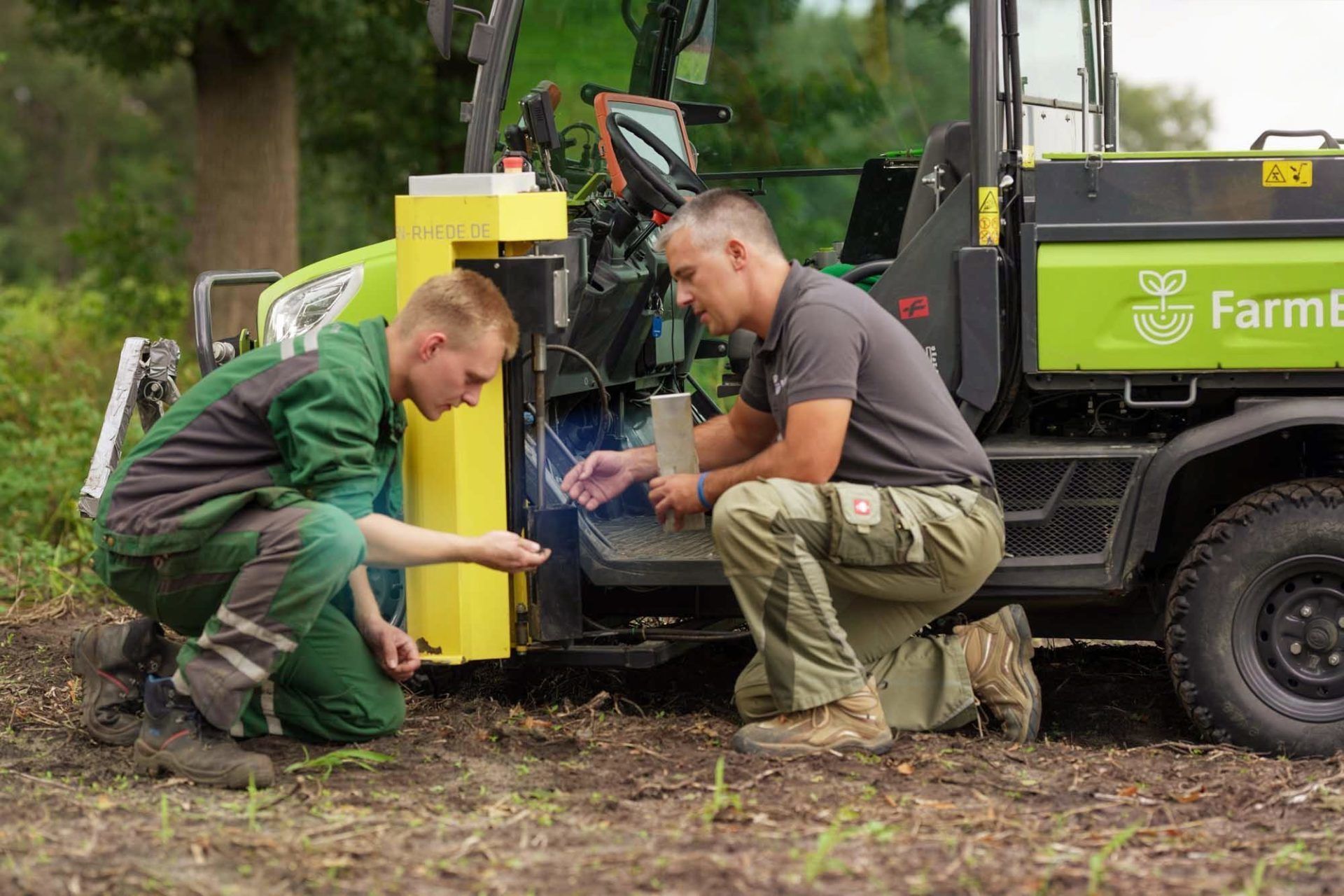 Zwei Männer arbeiten auf einem Feld an einem Traktor.