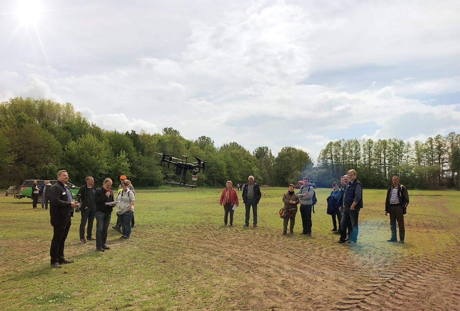 Eine Gruppe von Menschen steht auf einem Feld, im Hintergrund ist eine Drohne zu sehen.