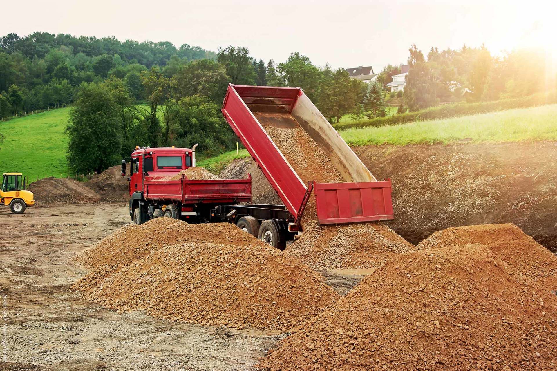Ein roter Muldenkipper kippt auf einer Baustelle Erde auf einen Haufen.