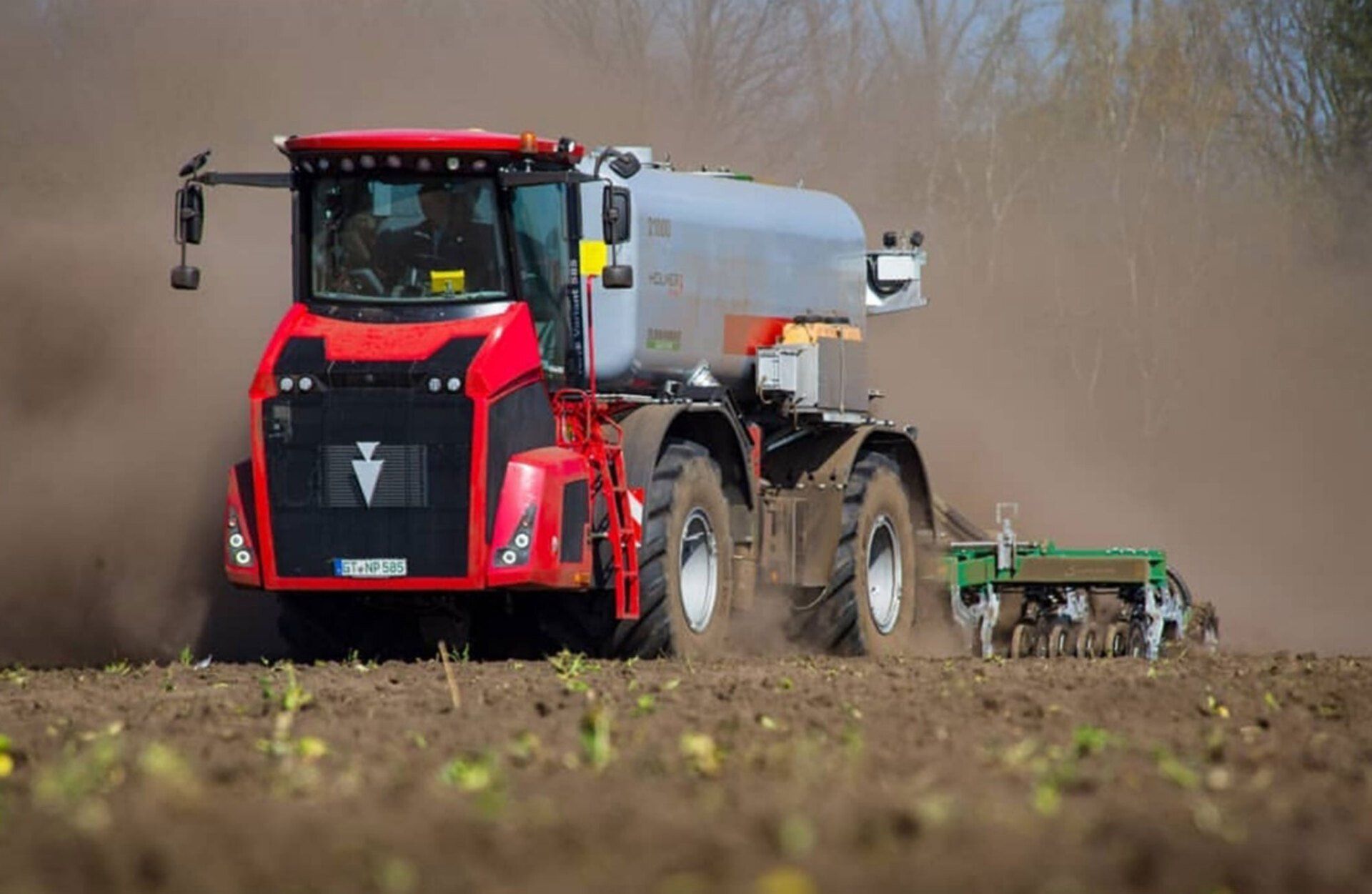 Ein roter Traktor pflügt ein Feld, an dem eine grüne Sämaschine befestigt ist.
