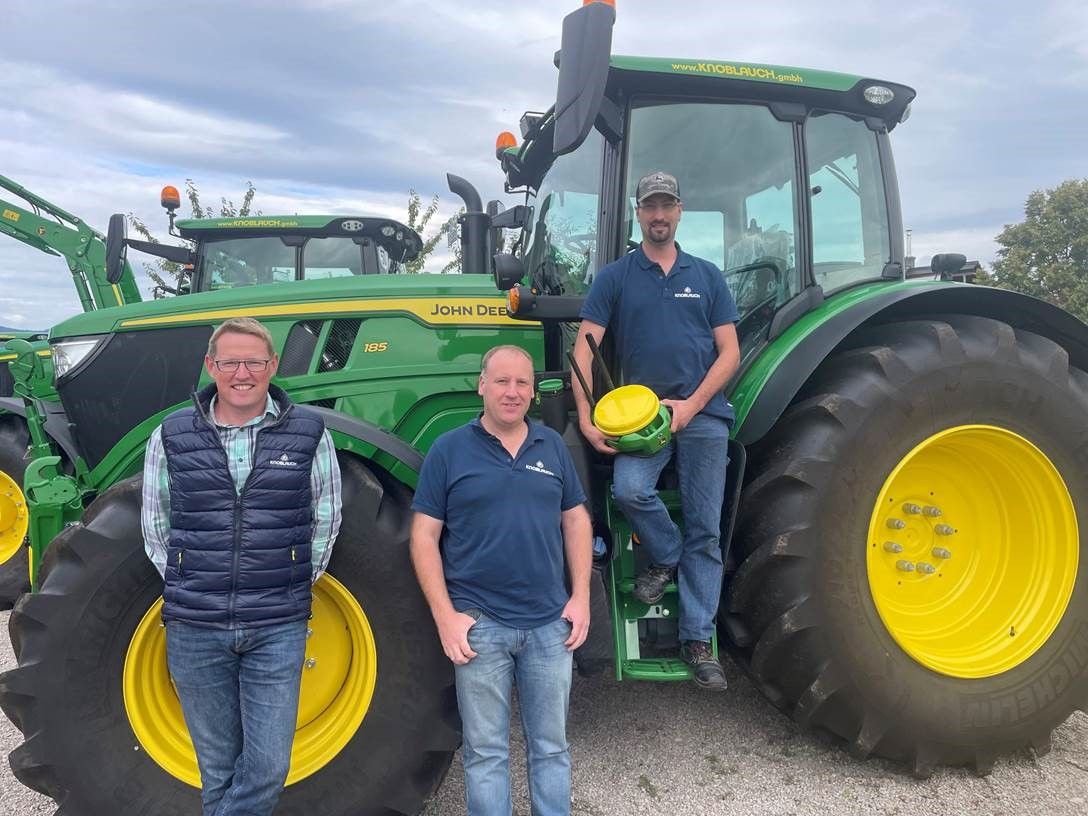 Drei Männer stehen vor einem grünen John Deere Traktor.