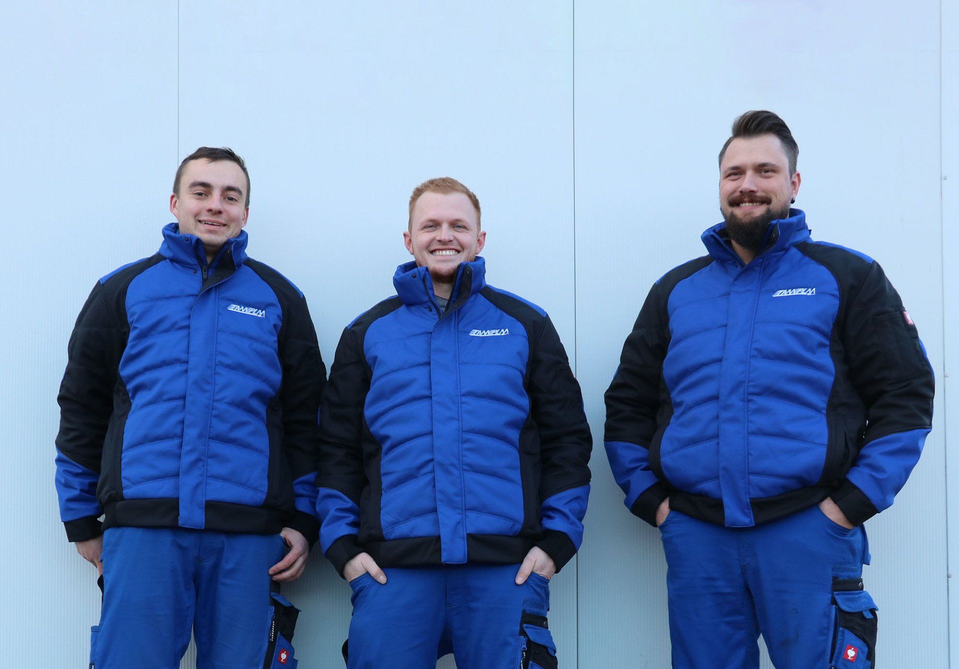 Drei Männer in blauen Jacken und blauen Hosen stehen nebeneinander.