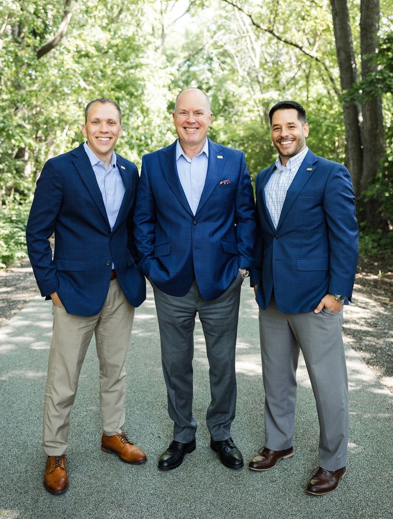 Three men in business attire standing indoors, smiling.