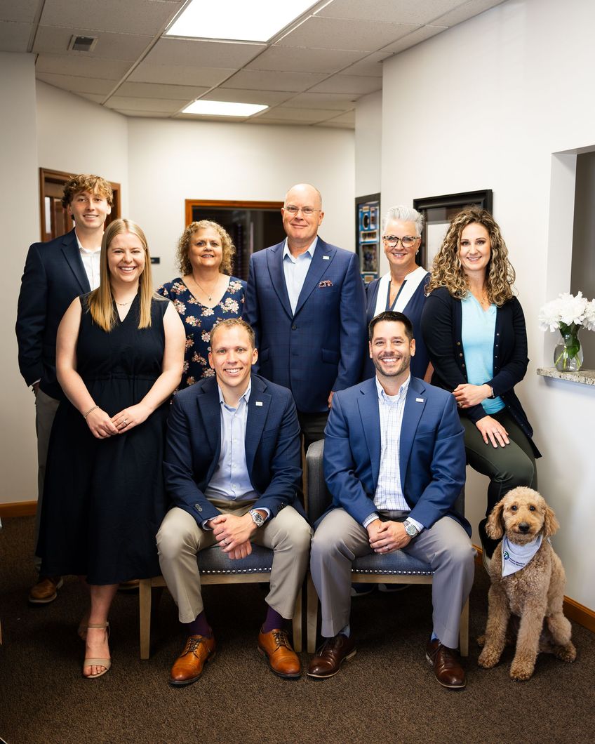 Group of seven people posing for a photo in an office setting with a dog.