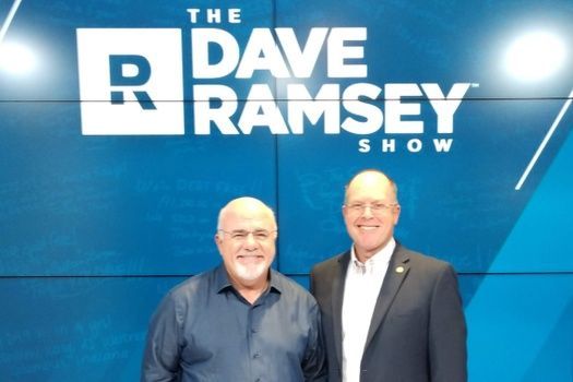 Two men stand in front of a blue backdrop with 