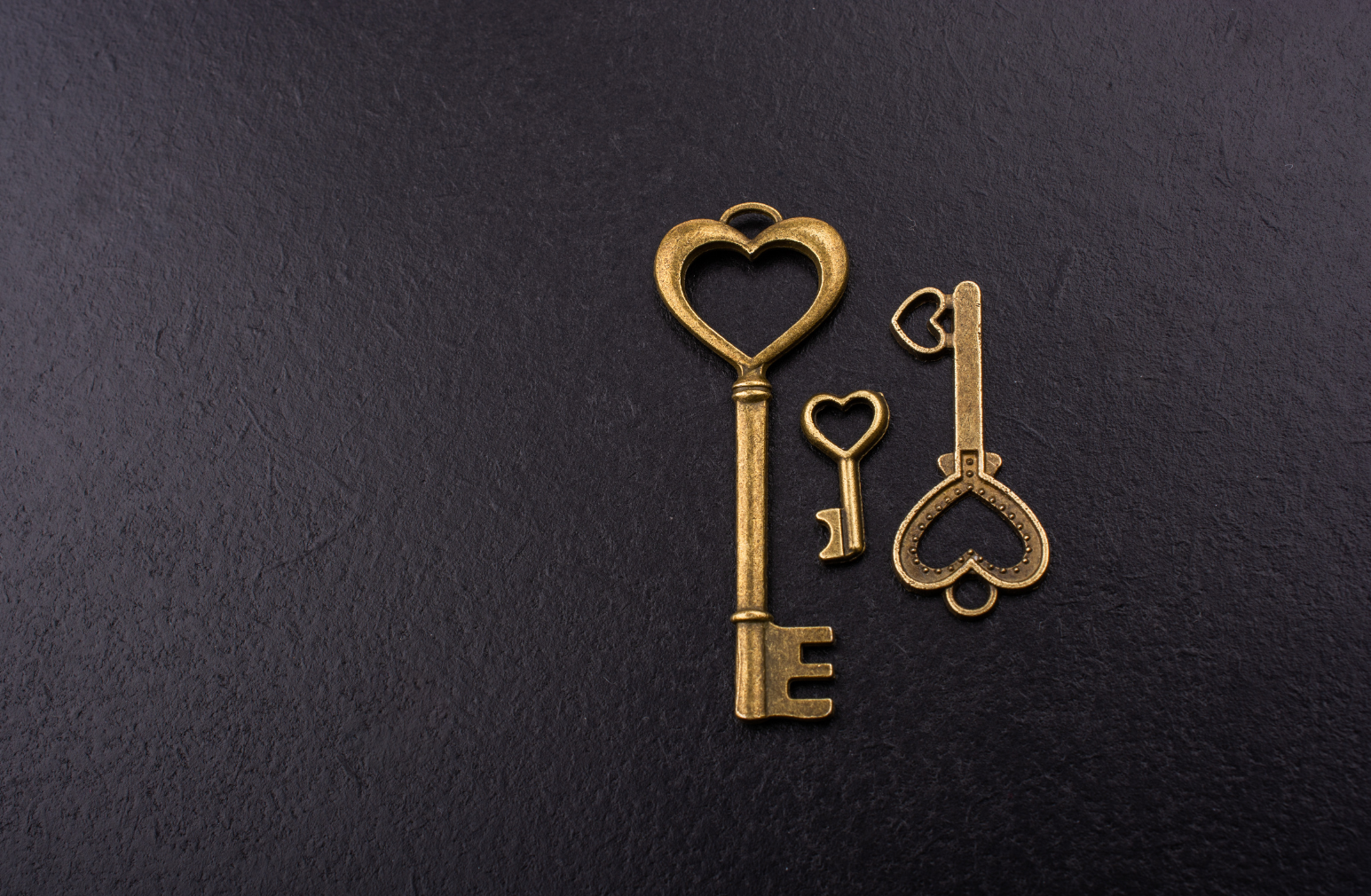 Three gold keys with hearts on them on a black background