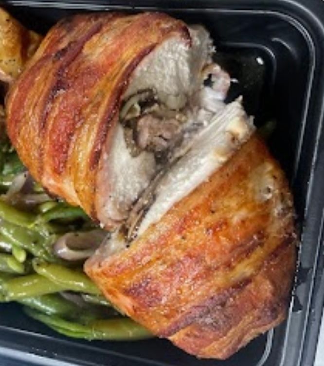 A close up of a chicken wrapped in bacon next to green beans