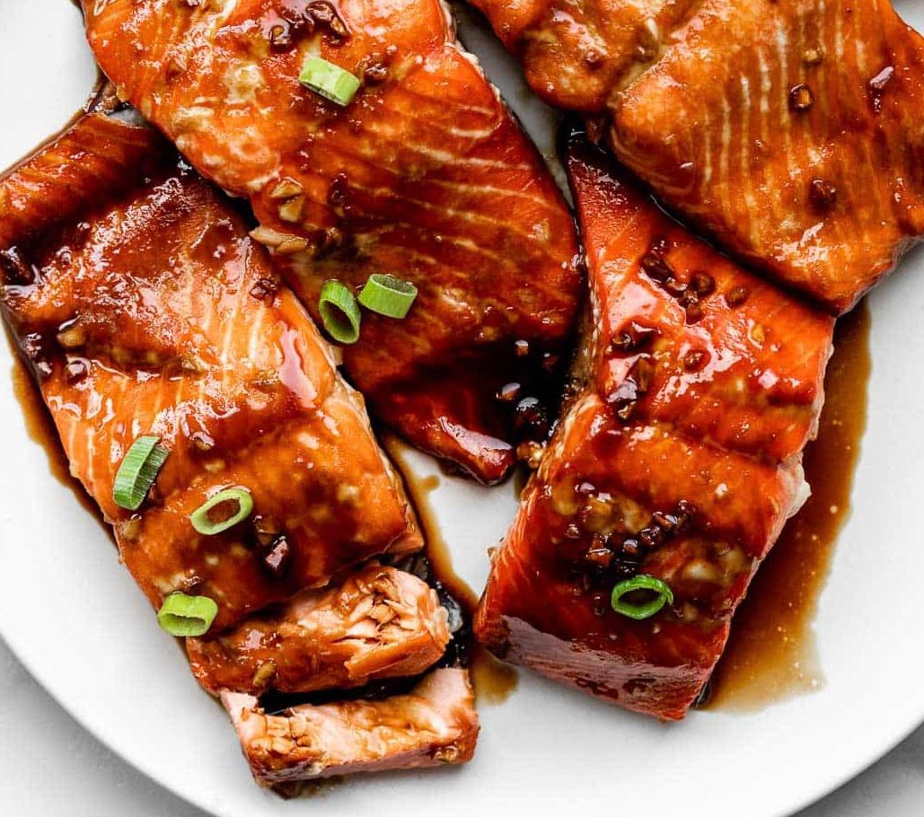 A white plate topped with slices of salmon covered in sauce and green onions.