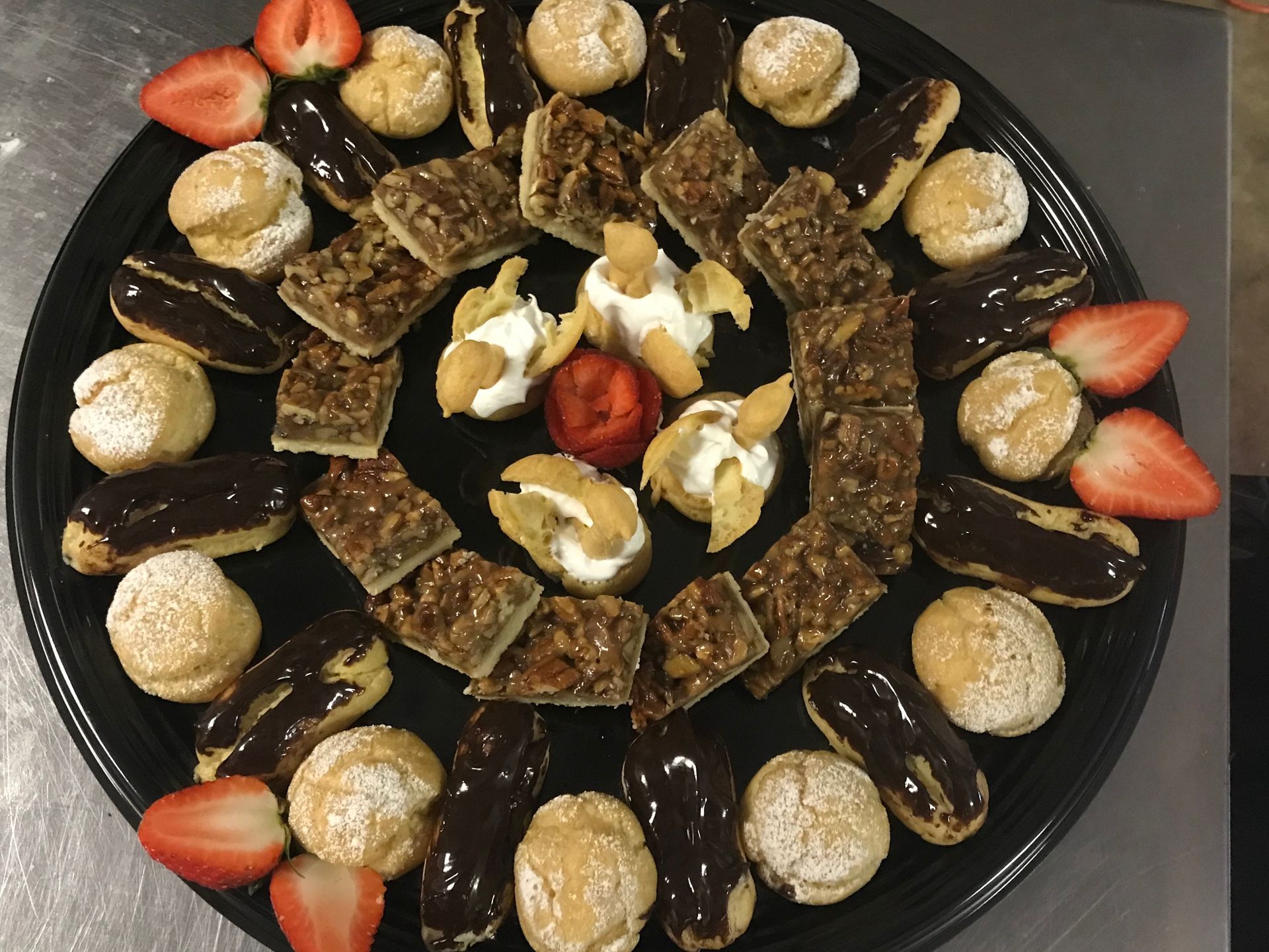 A black plate topped with a variety of desserts and strawberries