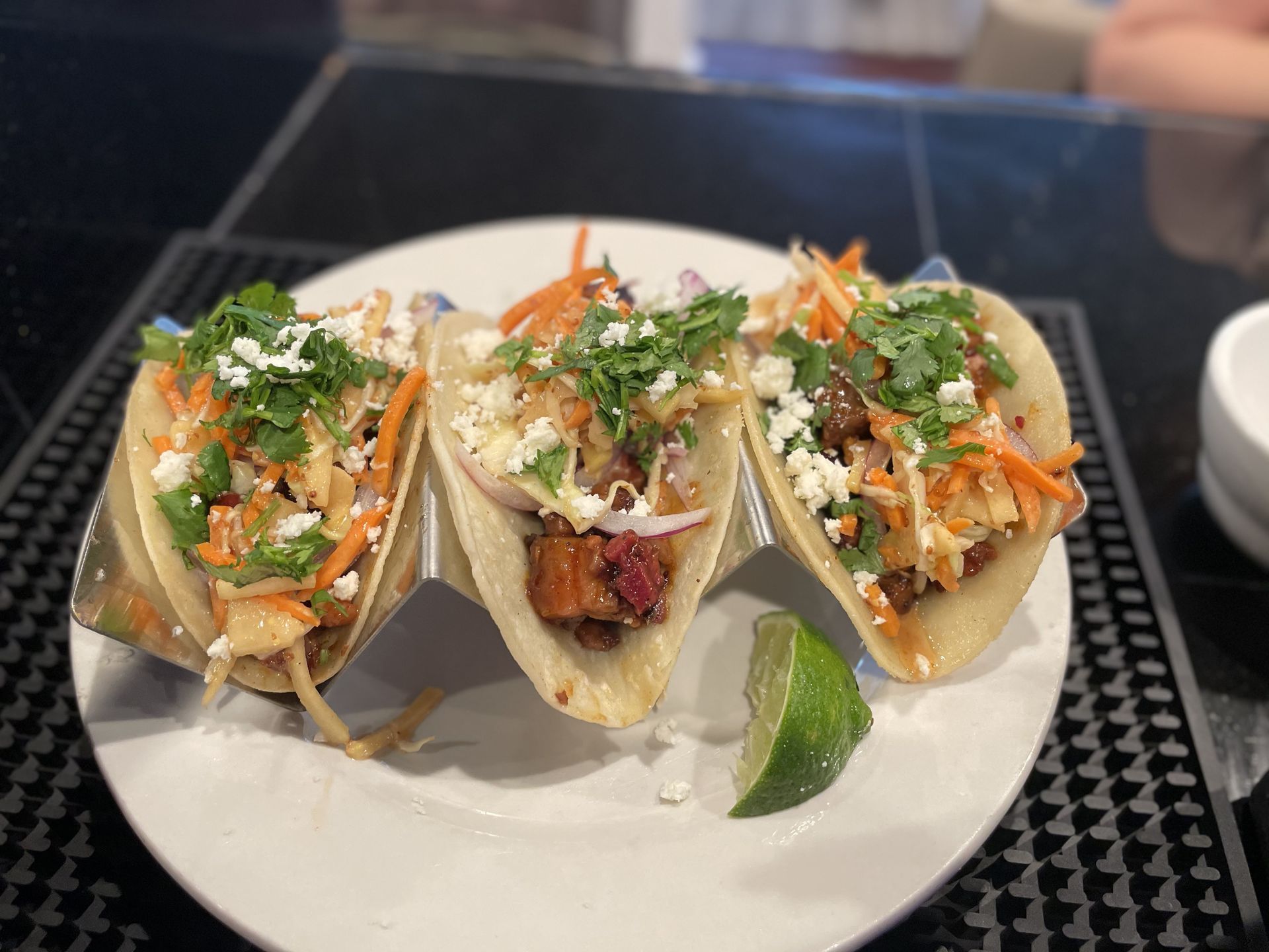 A white plate topped with three tacos and a lime.