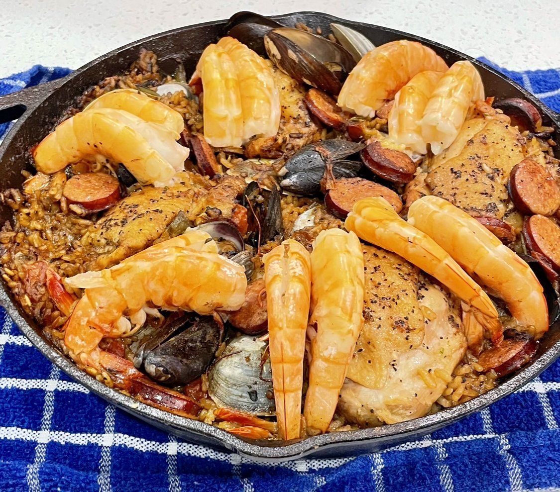 A skillet filled with seafood and rice on a blue and white checkered towel.