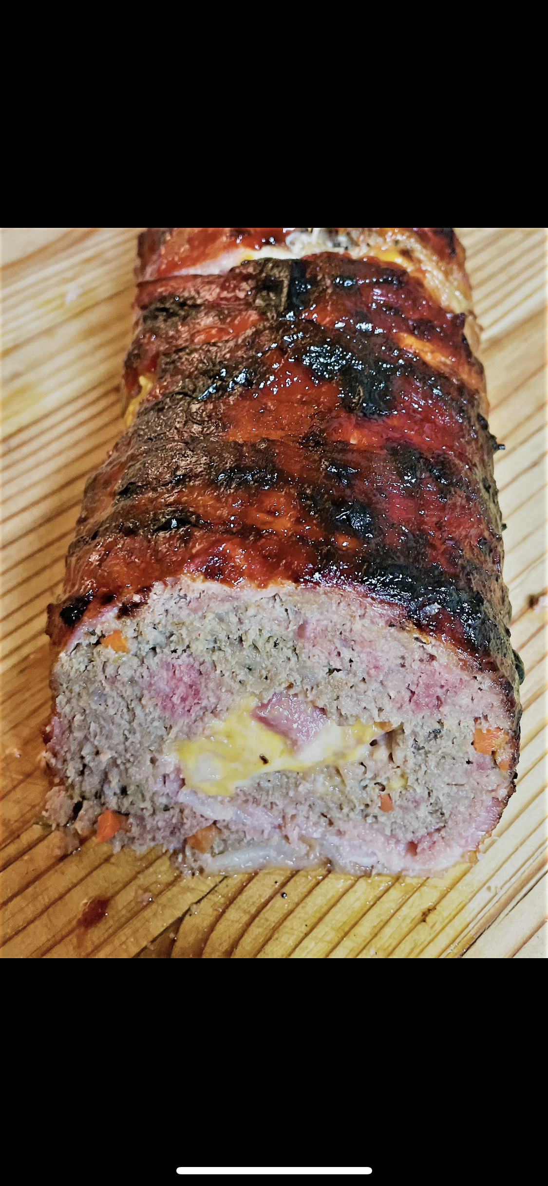 A meatloaf wrapped in bacon is sitting on a wooden cutting board.