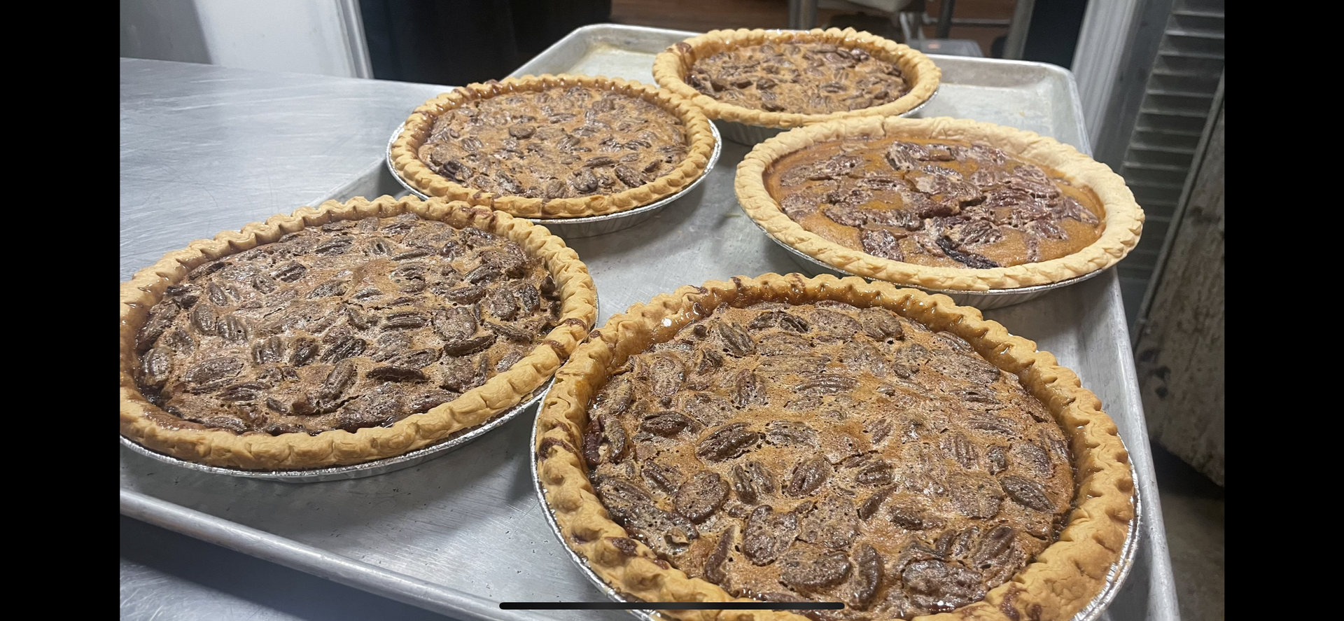 Four pecan pies are sitting on a metal tray.