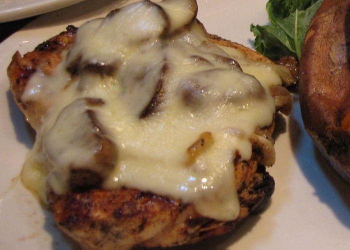 A chicken sandwich with mushrooms and cheese on a white plate