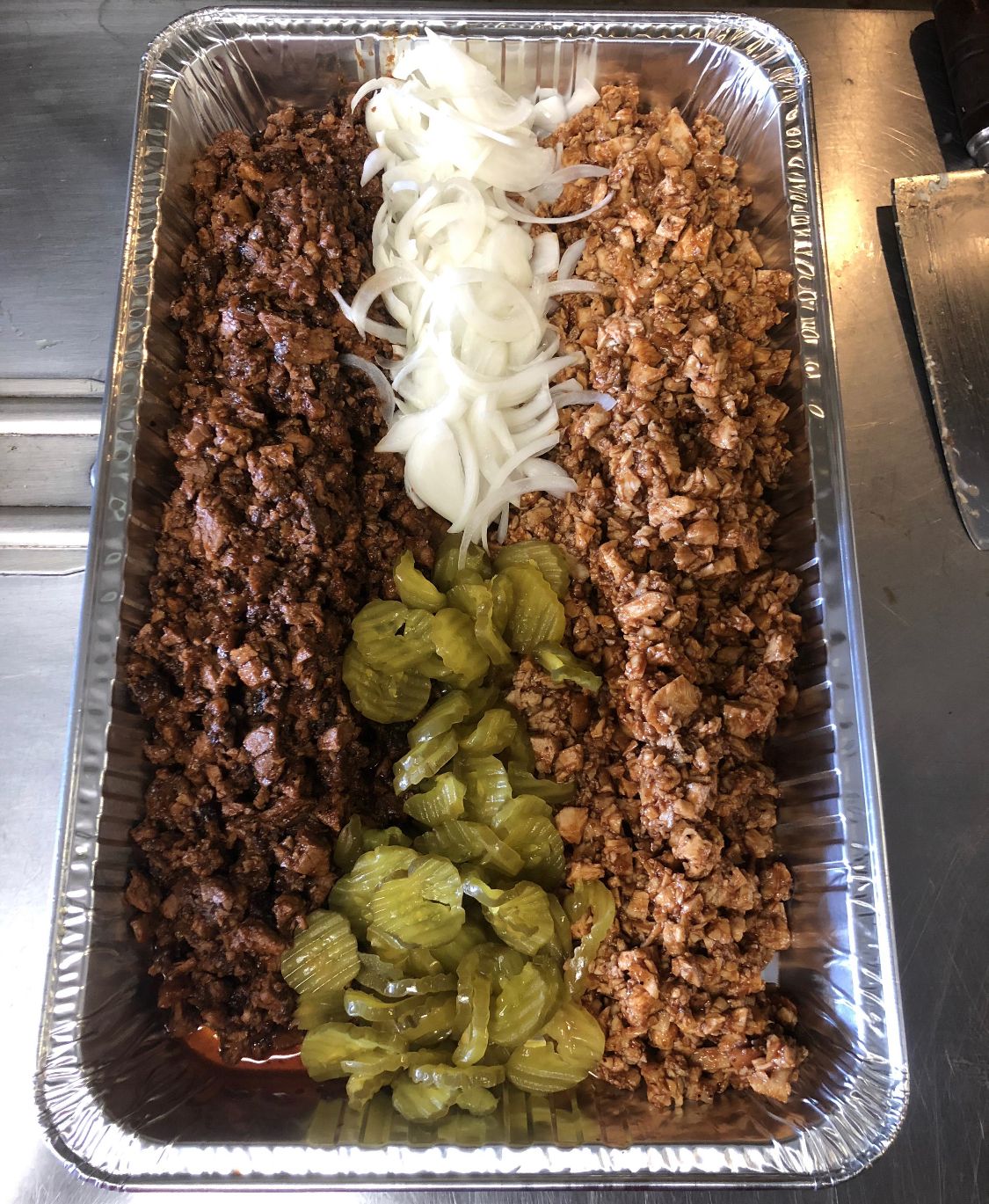 A tray of food with meat , pickles and onions on a table.
