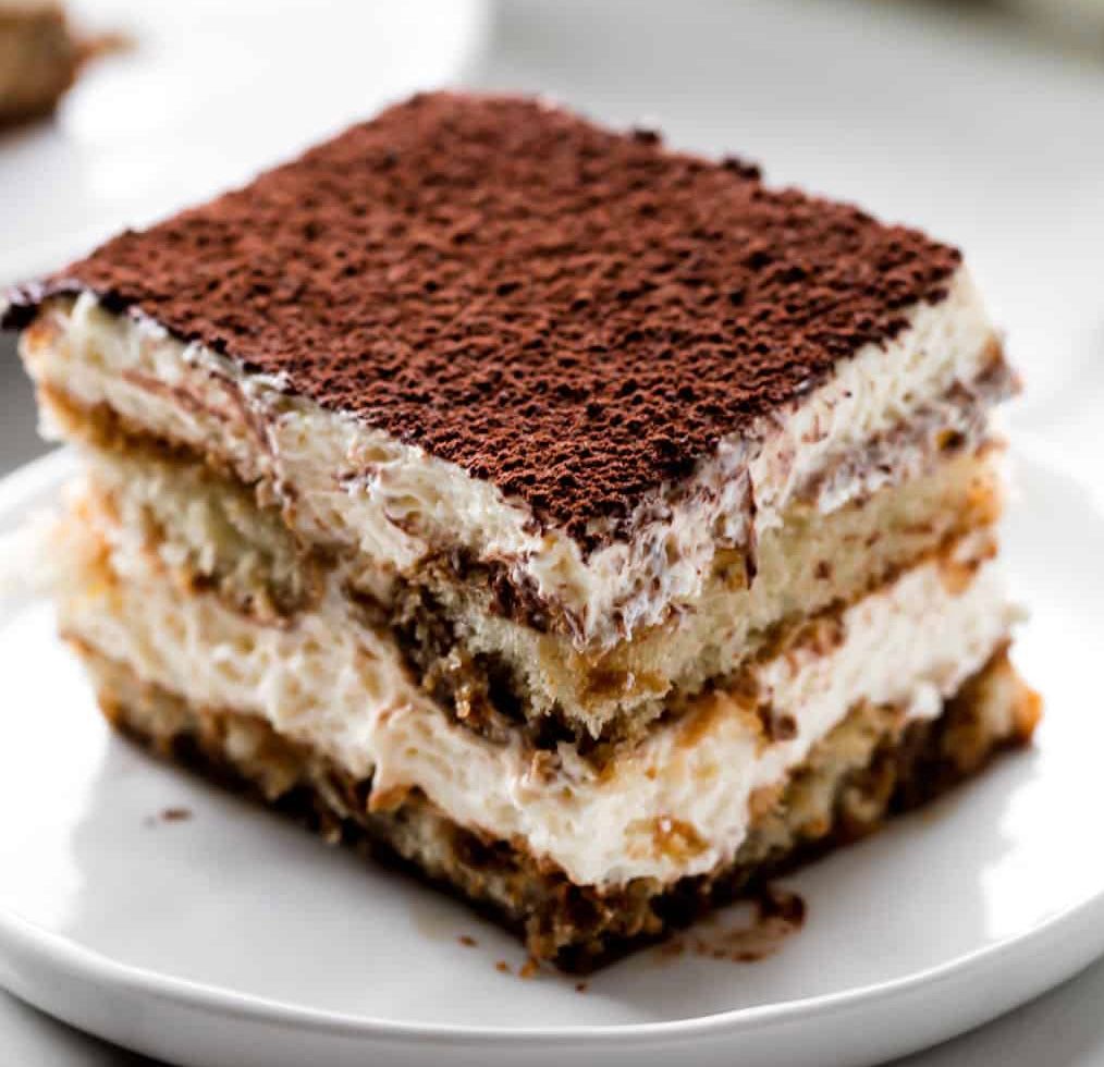 A piece of tiramisu cake on a white plate.