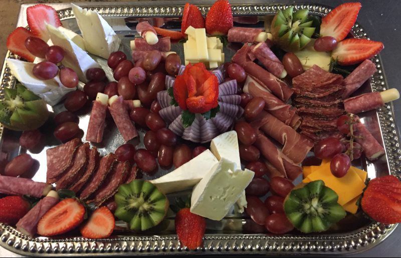 a tray of meats , cheeses , grapes and strawberries on a table