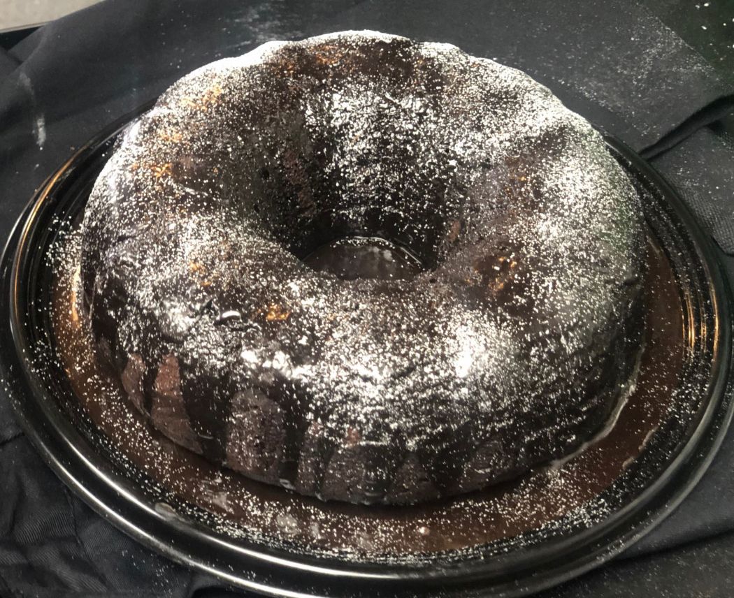A chocolate bundt cake covered in powdered sugar on a black plate