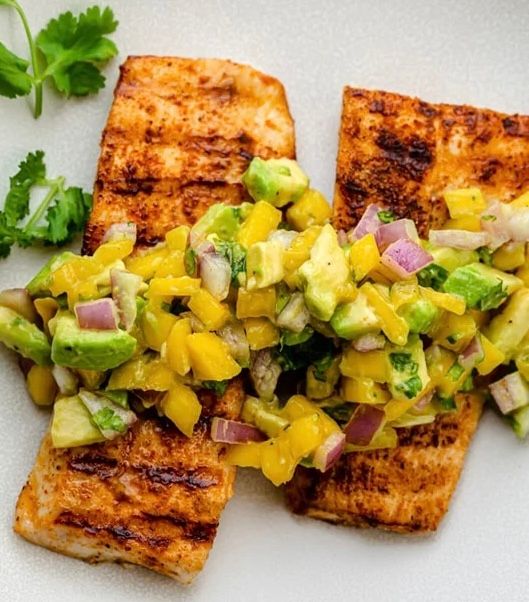 A white plate topped with grilled salmon and avocado salsa