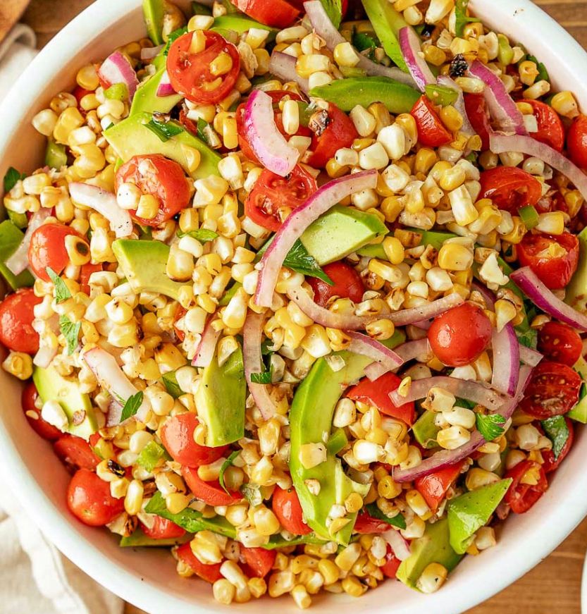 A bowl of corn salad with tomatoes , onions , and avocado.