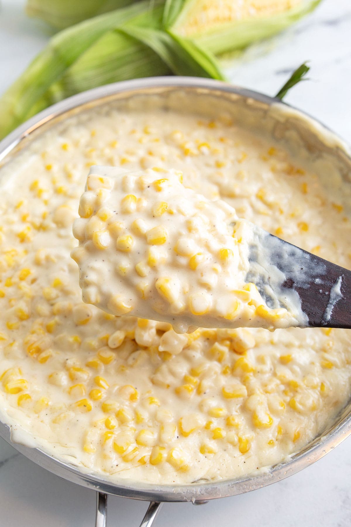 A spoonful of creamed corn is being scooped out of a pan.