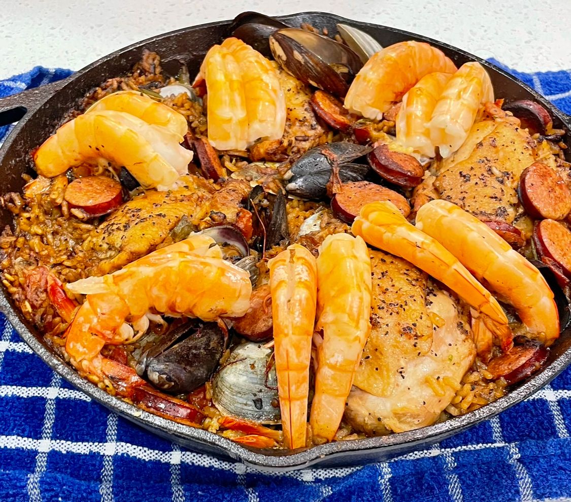A skillet filled with shrimp , chicken , mussels and sausage on a blue towel.