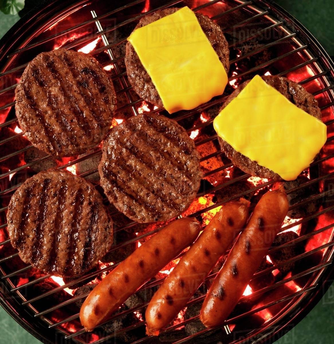 Hamburgers and hot dogs are cooking on a grill