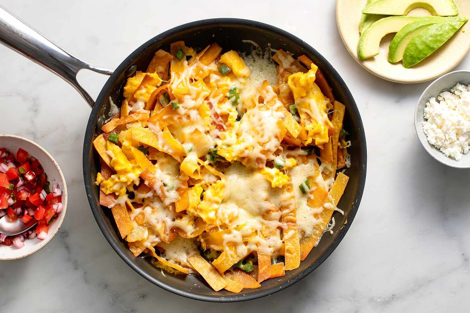 A pan filled with tortilla chips , eggs , cheese and avocado.