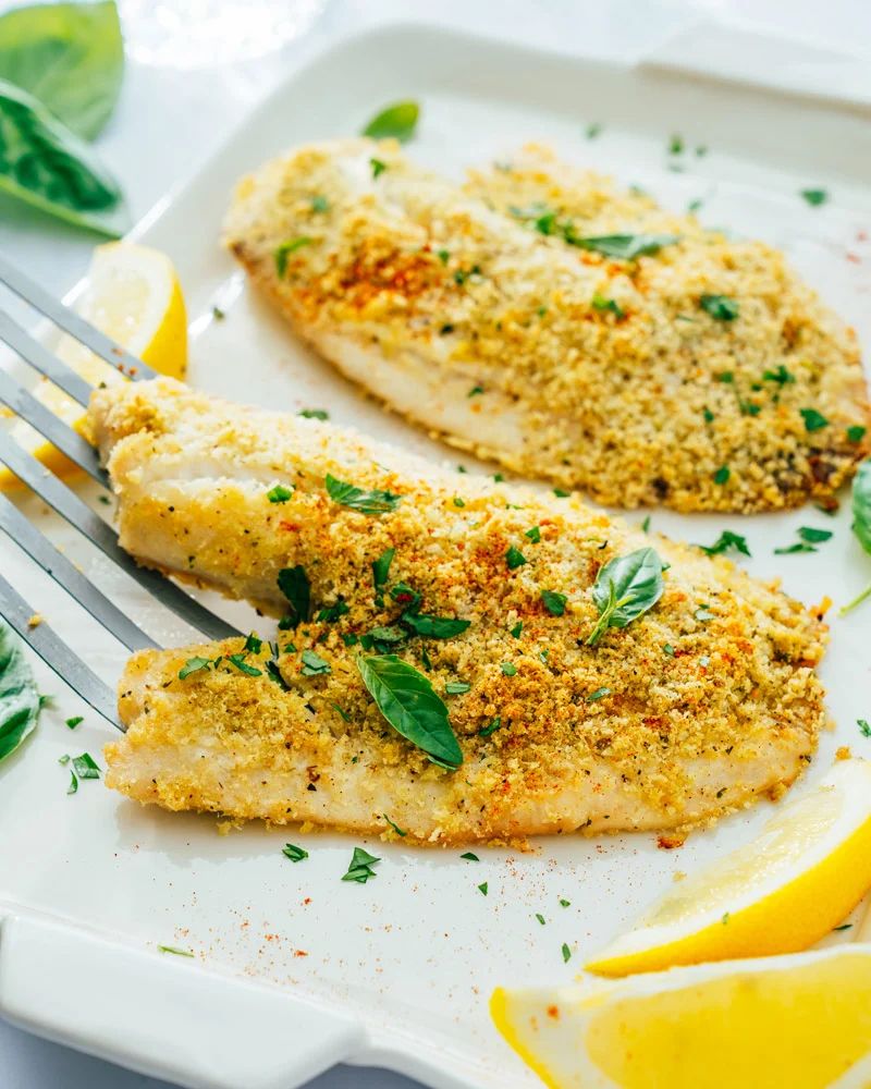 A white plate topped with breaded fish and lemon slices with a fork.