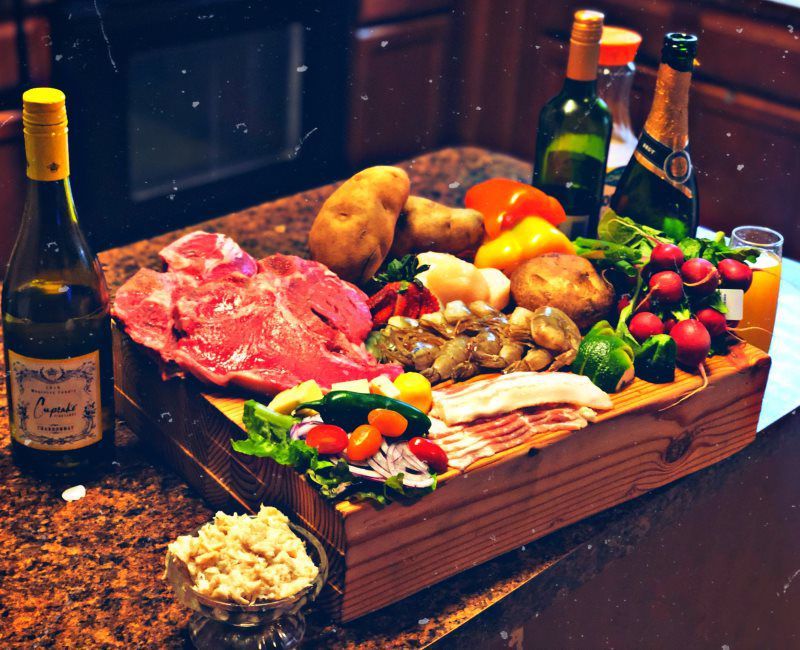 a wooden cutting board filled with meat and vegetables next to a bottle of wine