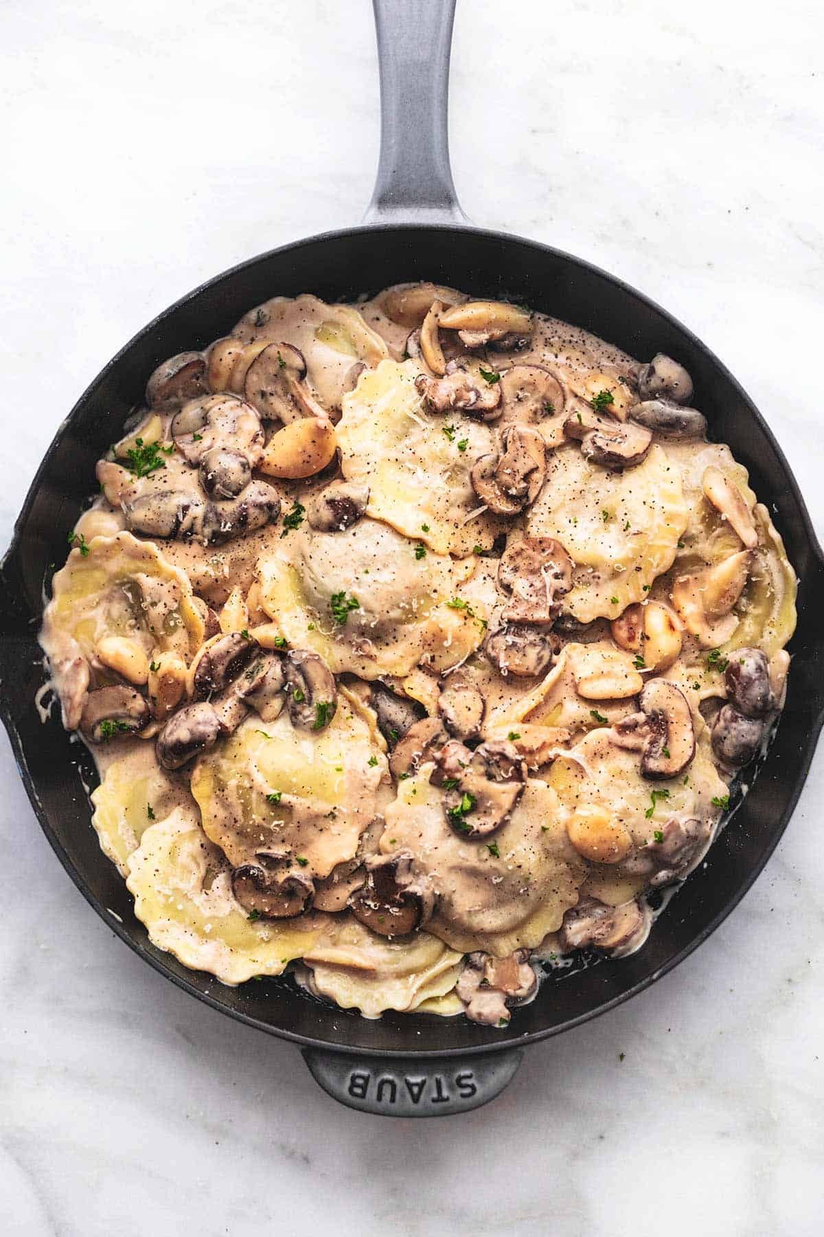 A skillet filled with ravioli and mushrooms on a table.