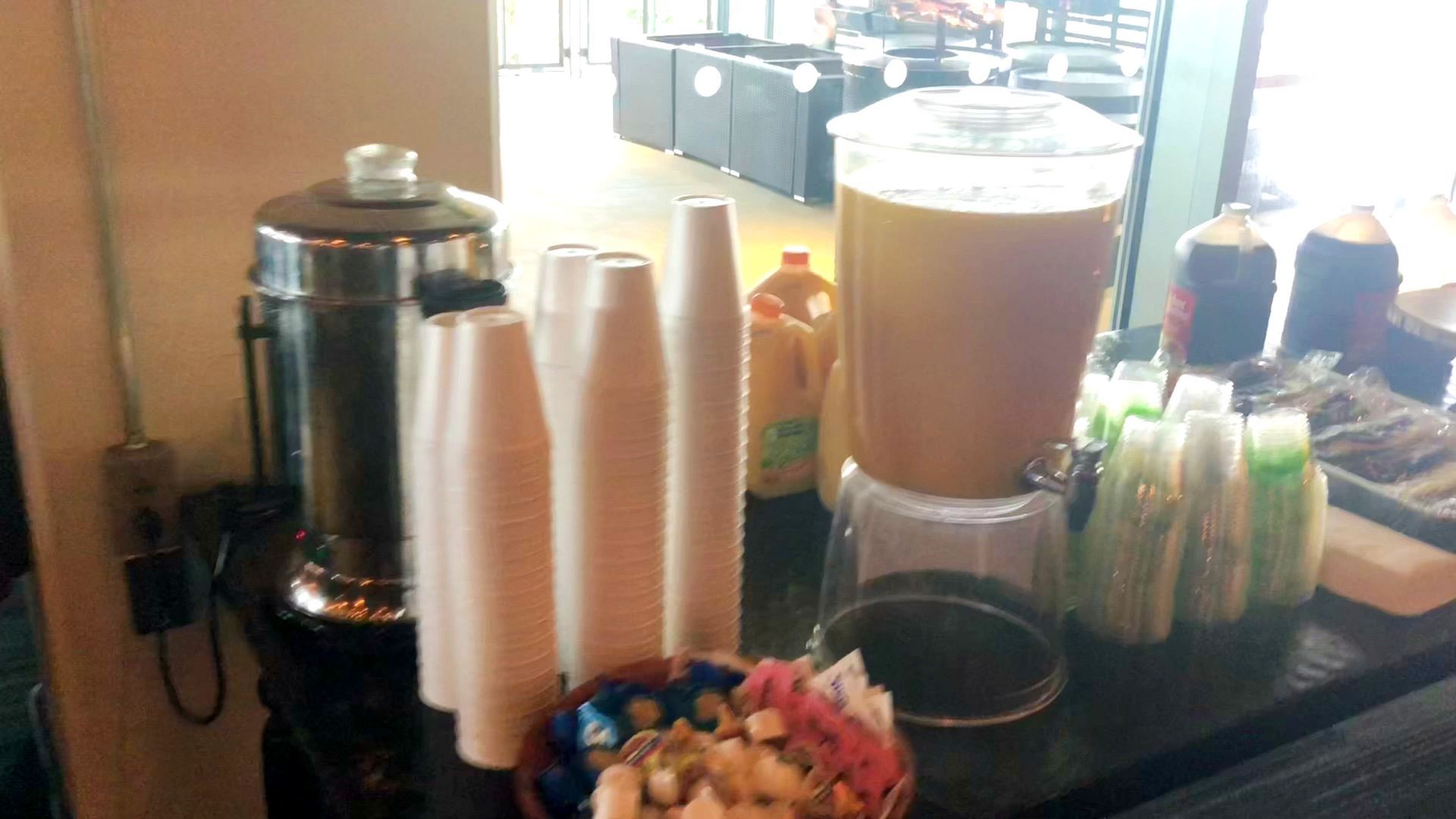 A table with a drink dispenser , cups , and a bowl of snacks.