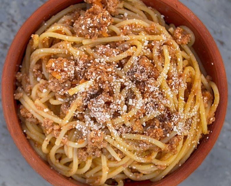 A bowl of spaghetti with meat sauce and cheese on top.
