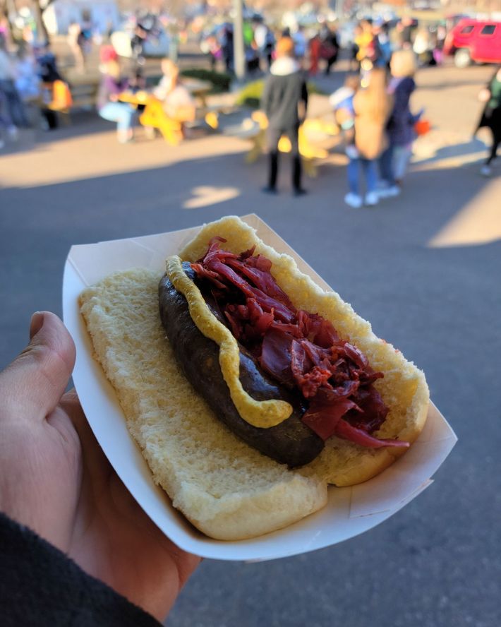 A person is holding a hot dog in a paper container.